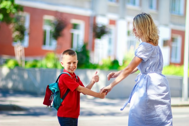 Eine glückliche Mama führt das Kind auf dem Rückweg zur Schule