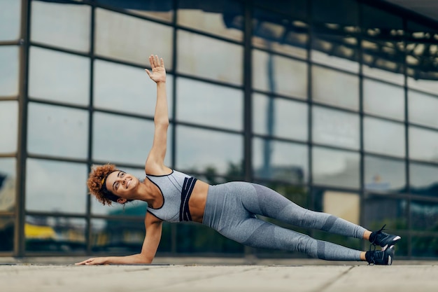 Eine glückliche, motivierte Sportlerin mit lockigem Haar, die Seitenplanken und Aufwärmübungen macht