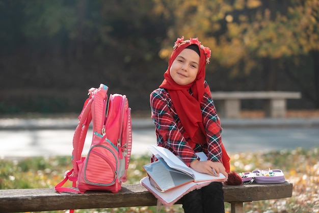 Eine glückliche muslimische Studentin, die im Herbstpark für die Schule lernt.