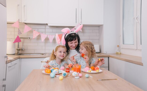 Eine glückliche Mutter hat Spaß mit ihren kleinen Töchtern, indem sie Ostereier färbt Frohe Ostern