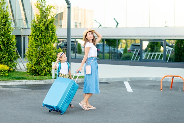 Eine glückliche Mutter mit einem Kind mit blauem Koffer fährt in den Urlaub oder auf eine Reise und fährt zum Flughafen