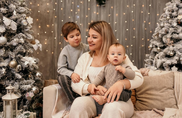 Eine glückliche Mutter mit ihren Söhnen sitzt auf dem Sofa in einem Raum in Neujahrsatmosphäre