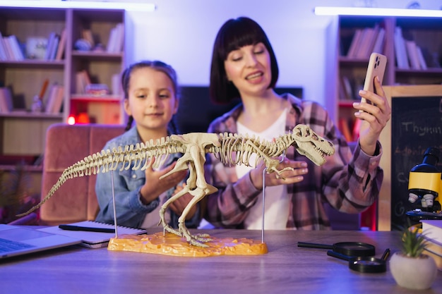 Eine glückliche Mutter untersucht das Skelett eines Dinosauriers mit einer klugen, niedlichen Tochter