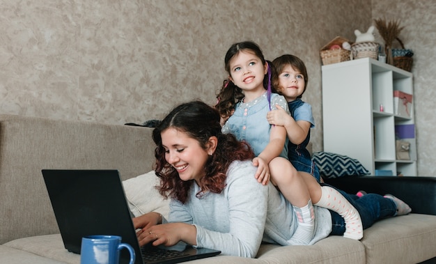 Eine glückliche Mutter versucht gleichzeitig mit ihren Kindern zu arbeiten und zu spielen.