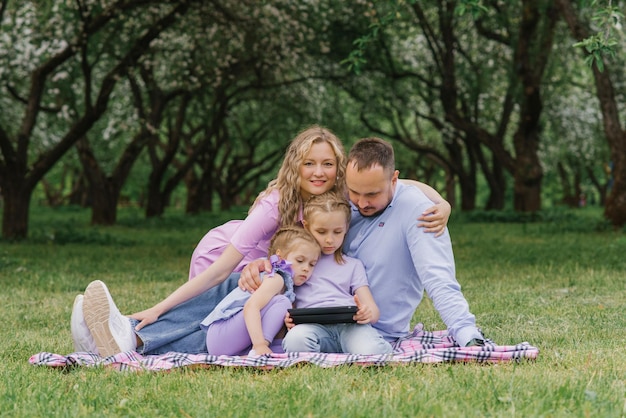 Eine glückliche schöne Familie sitzt im Sommer auf einer Decke im Park und schaut sich die Decke an und spricht per Videolink