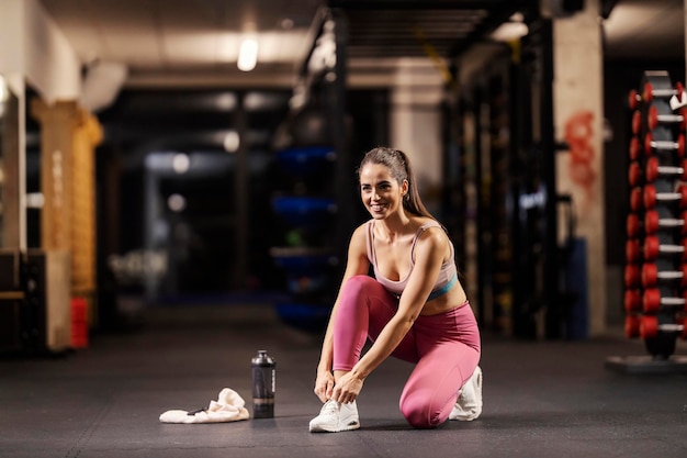 Eine glückliche Sportlerin bindet sich im Fitnessstudio die Schnürsenkel und bereitet sich auf das Training vor