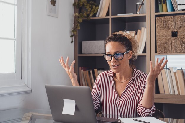 Eine glückliche und fröhliche Geschäftsfrau, die in einer Videokonferenz von zu Hause aus mit Arbeitskollegen spricht und kommuniziert. Arbeiten vom Haussperrkonzept. Weibliche Person, die Computer verwendet.