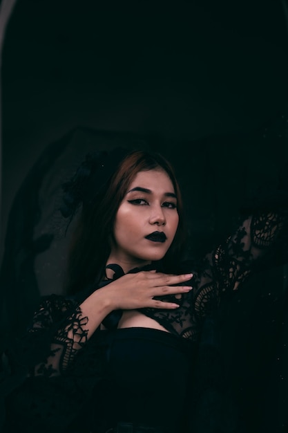 Eine gotische indonesische Frau, die einen schönen schwarzen Hut trägt, während sie sich wie eine Hexe in Schwarz kleidet