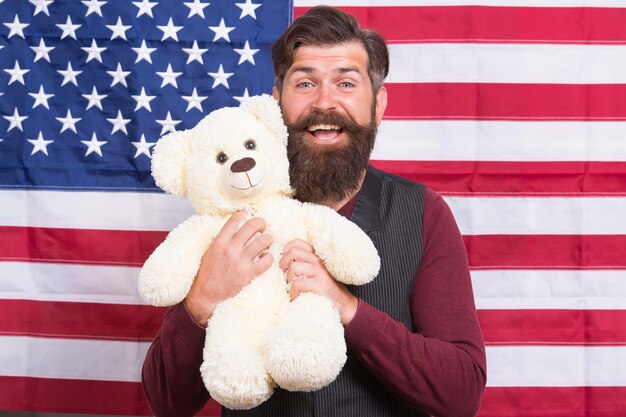 Eine große All-Glory-Flagge Glücklicher Hipster, der Teddybär auf amerikanischem Flaggenhintergrund hält Bärtiger Mann, der mit Stofftier und Nationalflagge der Vereinigten Staaten lächelt Wenn Sie sich gut fühlen, lassen Sie Ihre Flagge fliegen