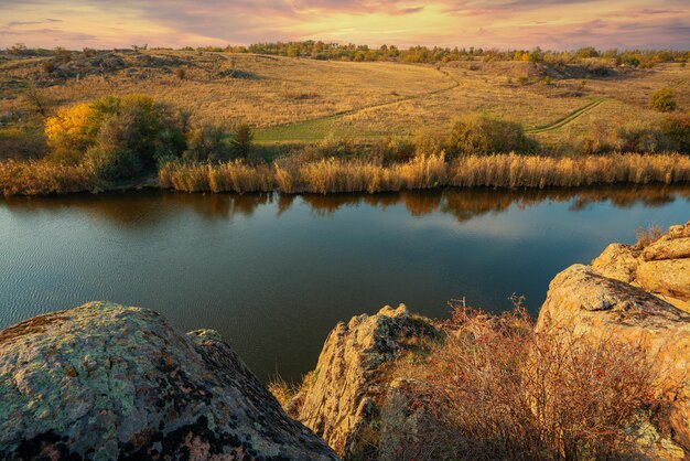 Eine große Anzahl von mit grüner Vegetation bedeckten Steinmineralien, die über einem kleinen Fluss in der malerischen Ukraine und ihrer wunderschönen Natur liegen