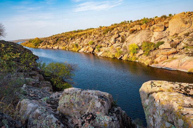 Eine große Anzahl von Steinmineralien, die mit grüner Vegetation bedeckt sind, liegen über einem kleinen Fluss in der malerischen Ukraine und ihrer wunderschönen Natur