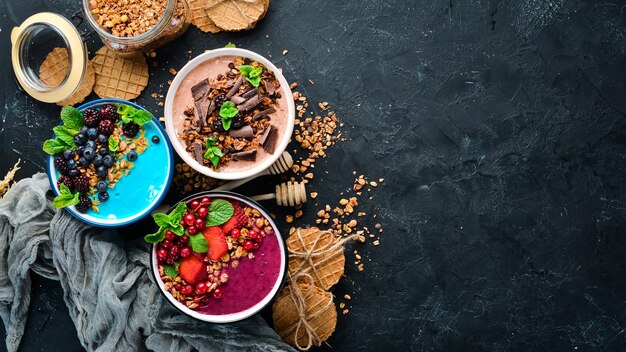 Eine große Auswahl an farbigen Frucht-Smoothies mit Joghurt, frischem Obst und Beeren Ein gesundes Frühstück Draufsicht Freier Platz für Ihren Text Auf schwarzem Hintergrund