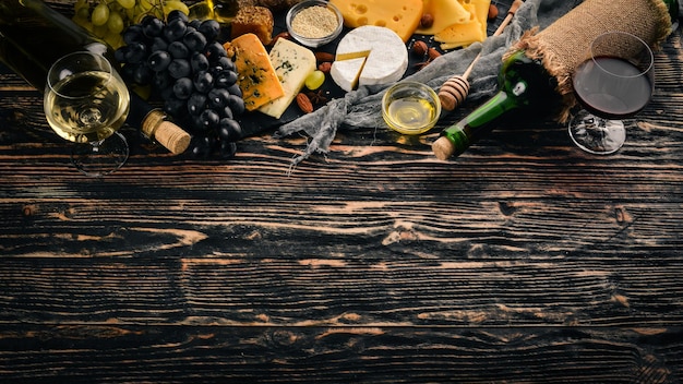 Eine große Auswahl an Käse Brie-Käse Gorgonzola Blauschimmelkäse Trauben Honig Nüsse Rot- und Weißwein auf einem Holztisch Ansicht von oben Freier Platz für Text