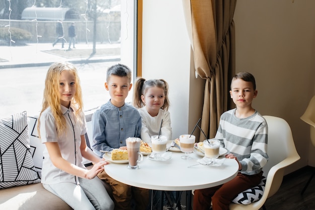 Eine große, freundliche Gesellschaft von Kindern feiert den Urlaub in einem Café mit einem köstlichen Dessert. Der Tag der Geburt.