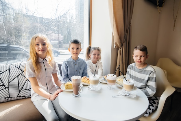 Eine große freundliche Gesellschaft von Kindern feiert den Urlaub in einem Café mit einem köstlichen Dessert. Der Tag der Geburt.