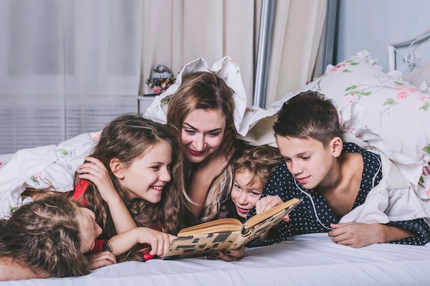 Eine große glückliche Familie. Mama liest ihren Kindern im Bett ein Buch vor, bevor sie schlafen gehen.