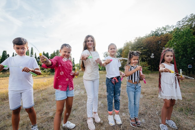 Eine große Gruppe fröhlicher Kinder spielt im Park und bläst Seifenblasen auf. Spiele in einem Kinderlager.