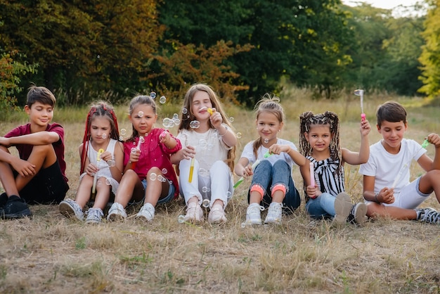 Eine große Gruppe fröhlicher Kinder spielt im Park und bläst Seifenblasen auf. Spiele in einem Kinderlager.