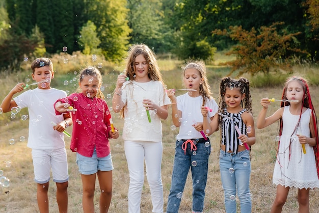 Eine große Gruppe fröhlicher Kinder spielt im Park und bläst Seifenblasen auf