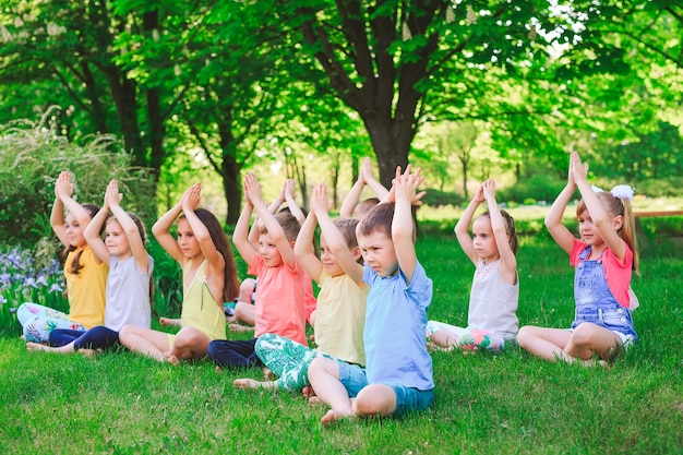 Eine große Gruppe Kinder nahm an Yoga im Park teil, der auf dem Gras sitzt.