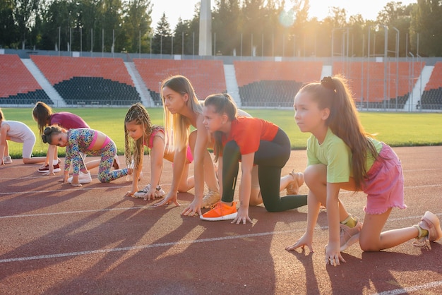 Eine große Gruppe von Mädchen wird am Start von einem Trainer unterrichtet, bevor sie bei Sonnenuntergang im Stadion laufen Ein gesunder Lebensstil