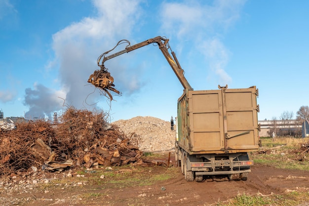 Eine große Maschine mit einem großen Stück Metall lädt einen Haufen Schrott in einen Müllcontainer