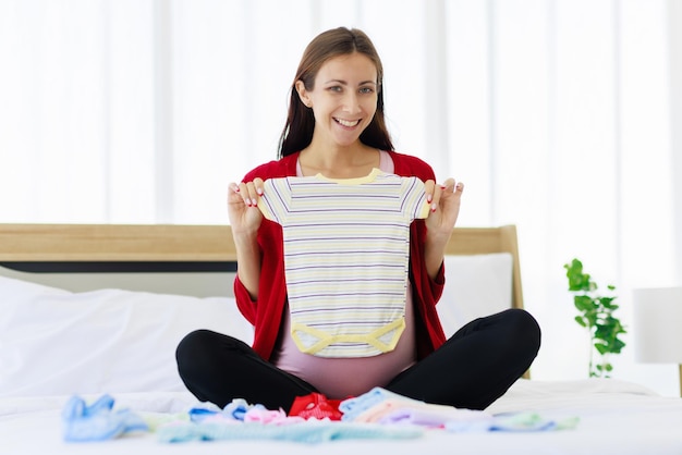 Eine große schwangere Frau bereitet glücklich Babykleidung auf ihrem Bauch vor