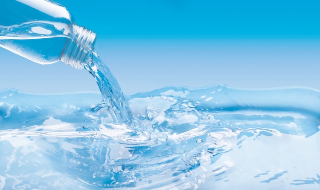 Eine große Wasserfläche und eine Glasflasche gießen Wasser mit Sprüheffekt. Blaue Farbwand mit Kopierraum.