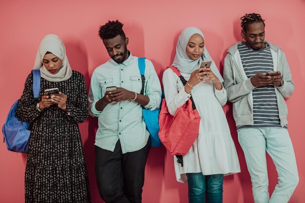 Eine Gruppe afrikanischer muslimischer Studenten, die Smartphones benutzen, während sie vor einem rosa Hintergrund stehen. Hochwertiges Foto