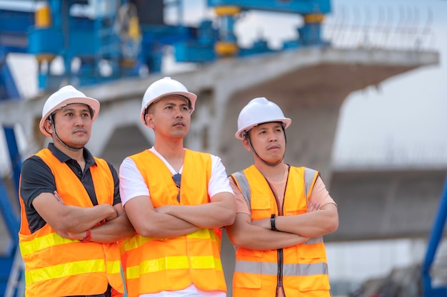 Eine Gruppe asiatischer Ingenieure diskutiert über die Arbeit am Standort des im Bau befindlichen Gebäudes Das Auftragnehmerteam bespricht die Gestaltung der Struktur. Drei Arbeiter arbeiten draußen