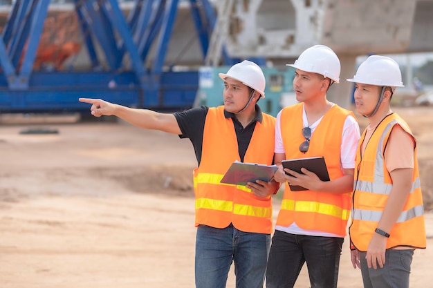 Eine Gruppe asiatischer Ingenieure diskutiert über die Arbeit am Standort des im Bau befindlichen Gebäudes Das Auftragnehmerteam bespricht die Gestaltung der Struktur. Drei Arbeiter arbeiten draußen