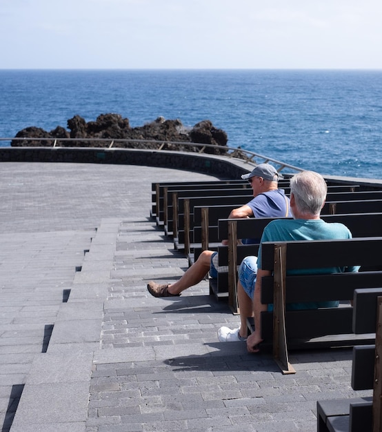 Eine Gruppe einsamer alter Menschen sitzt allein auf Bänken am Meer und schaut auf den Horizont über den Ozean