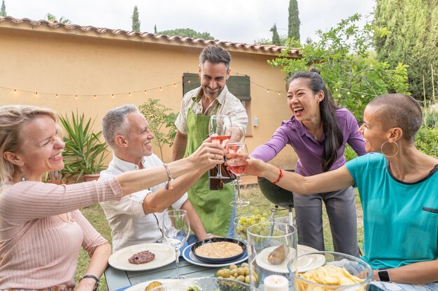 Eine Gruppe fröhlicher Freunde trinkt mit einem großen Lächeln um den Tisch im Haus-Patio-Diner