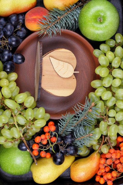 Eine Gruppe gesunder bunter Früchte und Beeren mit Tannenzweigen und einer Tonplatte auf dunklem Hintergrund Gemütliches Stillleben im Winter Ansicht von oben