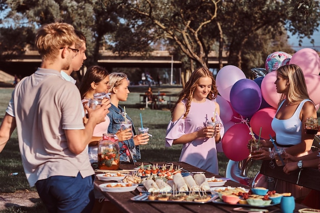 Eine Gruppe glücklicher Freunde, die gemeinsam Spaß haben und einen Geburtstag im Outdoor-Park feiern. Freunde sagen einen Toast auf der Picknickparty im Freien.