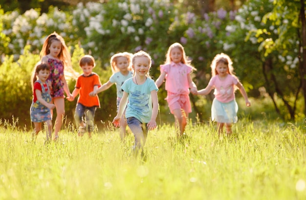 Eine Gruppe glücklicher Kinderjungen und Mädchen, die an einem sonnigen Sommertag im Park auf dem Gras laufen.