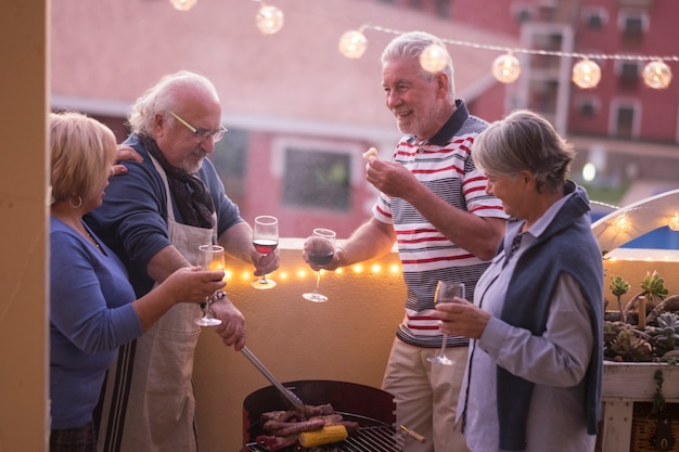 Eine Gruppe glücklicher Seniorenfreunde genießt zusammen eine Grillnacht zu Hause auf der Außenterrasse