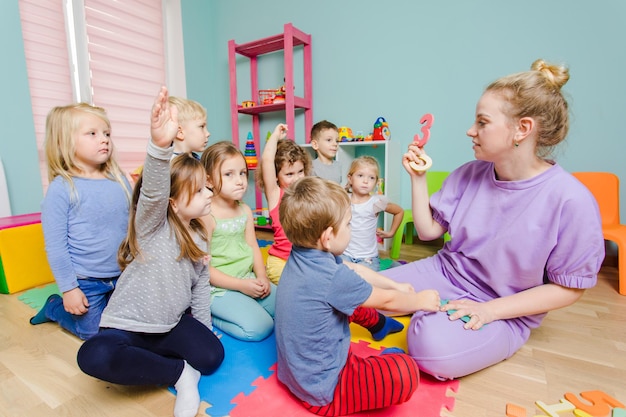 Eine Gruppe hübscher Kinder, die vor dem Lehrer auf einem Boden sitzen und aufmerksam zuhören Vorschulkinder lernen zu zählen