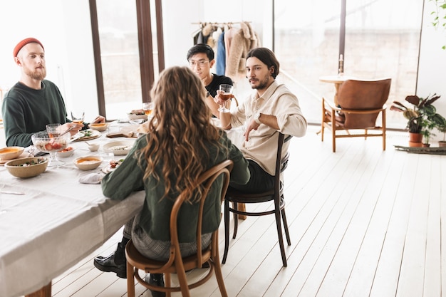 Eine Gruppe internationaler Freunde sitzt am Tisch voller Essen und redet nachdenklich miteinander