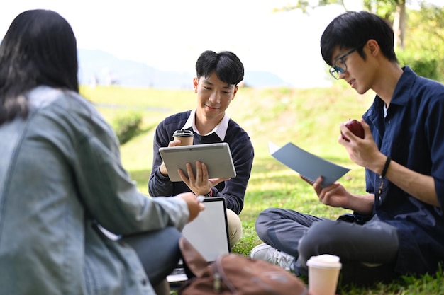 Eine Gruppe junger asiatischer College-Studenten, die darüber diskutieren, ihre Ideen auszutauschen und gemeinsam im Park zu arbeiten