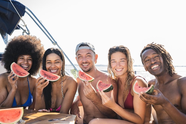 Eine Gruppe junger Freunde, die sich auf einer Luxusyacht entspannen, gemeinsam Spaß haben und auf einer privaten Party gesundes Obst essen, während sie im Seereise- und Yachtkonzept segeln