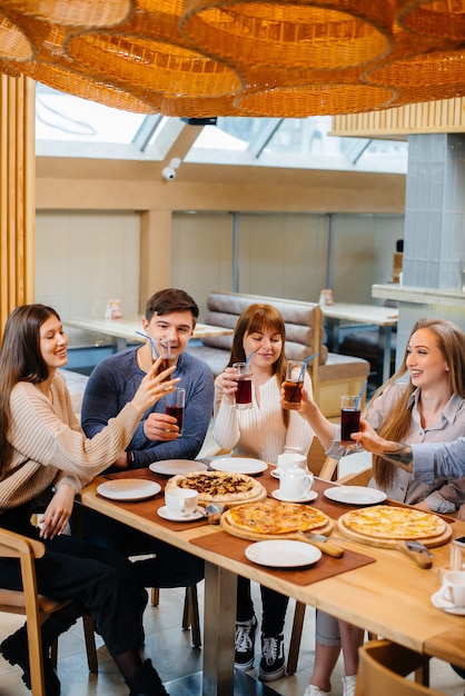 Eine Gruppe junger fröhlicher Freunde sitzt in einem Café und redet und isst Pizza. Mittagessen in der Pizzeria.