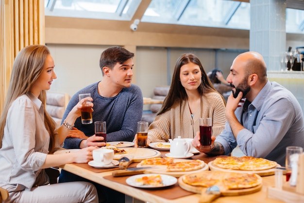 Eine Gruppe junger fröhlicher Freunde sitzt in einem Café und redet und isst Pizza. Mittagessen in der Pizzeria.