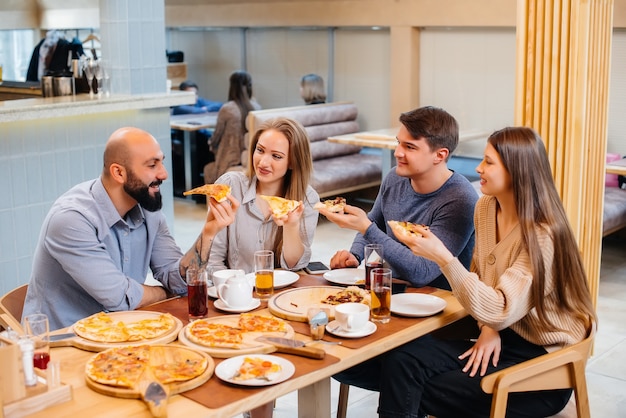 Eine Gruppe junger fröhlicher Freunde sitzt in einem Café und redet und isst Pizza