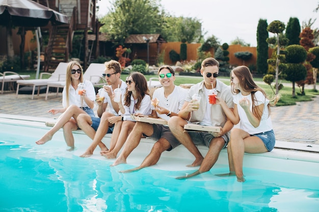 Eine Gruppe junger Leute, die sich auf einer Poolparty im Hinterhof amüsieren und sonnige Sommertage im Freien genießen, Cocktails trinken und Pizza und Sushi essen