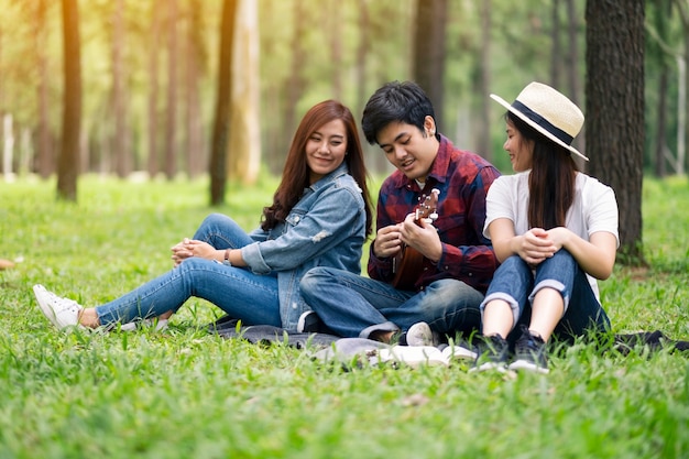 Eine Gruppe junger Leute, die Ukulele spielen, während sie zusammen im Wald sitzen