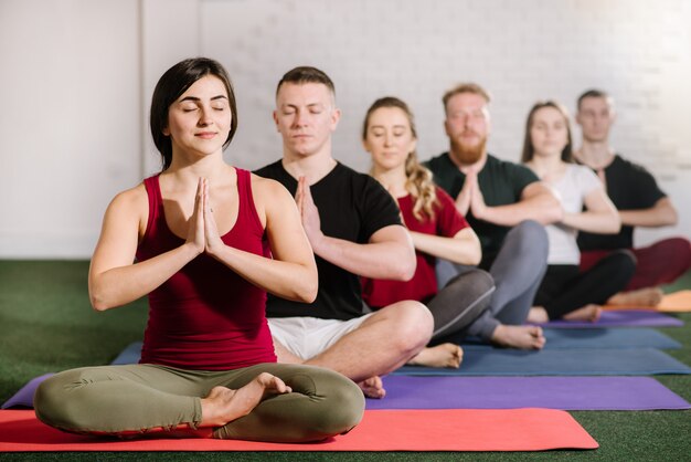 Eine Gruppe junger Menschen, die im Yoga sitzen, posieren hintereinander