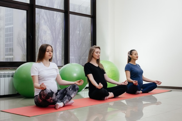Eine Gruppe junger schwangerer Mädchen macht Yoga und Sport auf Indoor-Matten. Gesunder Lebensstil.