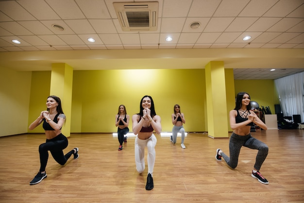 Eine Gruppe junger sportlicher Mädchen führt unter Anleitung eines Trainers Übungen im Fitnessstudio durch. Gesunder Lebensstil