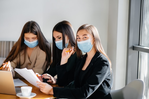 Eine Gruppe Mädchen in Masken sitzt in einem Café und arbeitet an Laptops